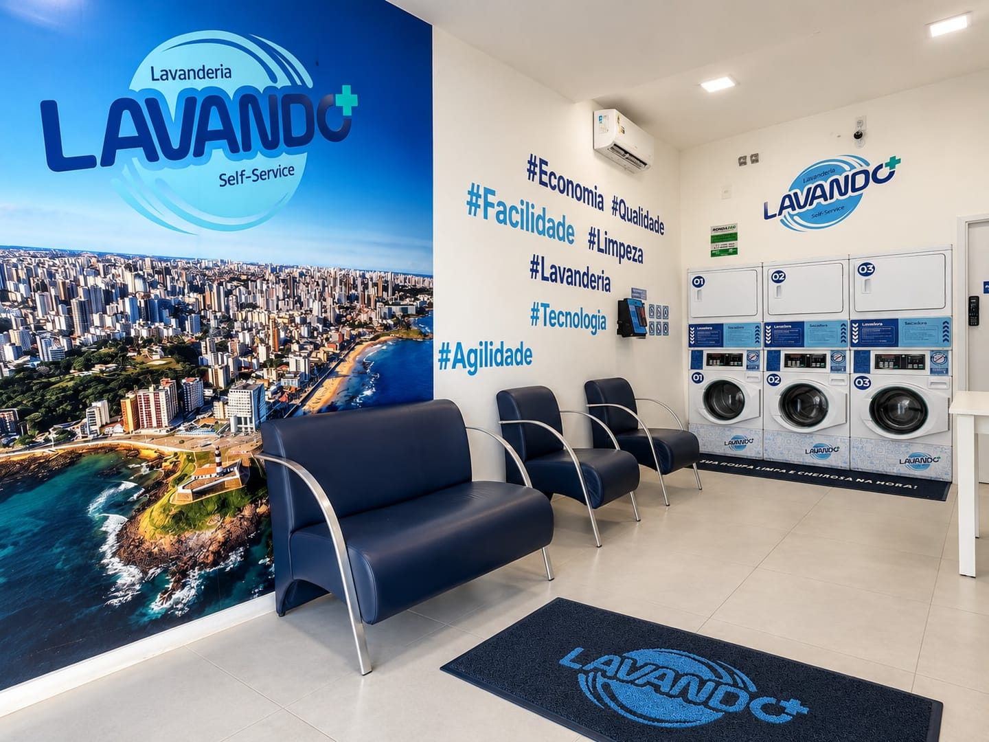 Sala de espera com poltronas azul-marinho, parede de hashtags, ar-condicionado, o totem de pagamento na parede e as máquinas de lavar e de secar ao fundo